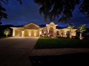 yellow home with palm trees and exterior lighting around the plants